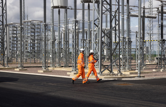 Two engineers wearing orange overalls and PPE in the Viking Link converter station AC yard