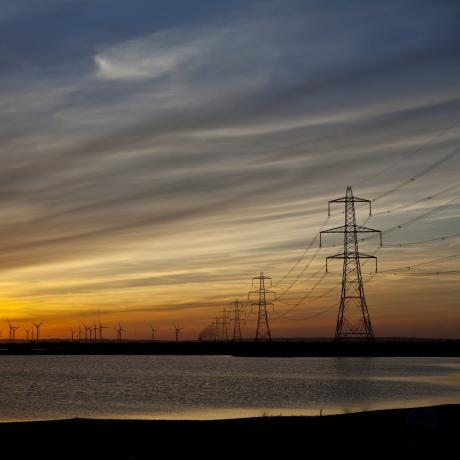 A beach at sunset with the sea coming in and electricity pylons dotted into the distance 